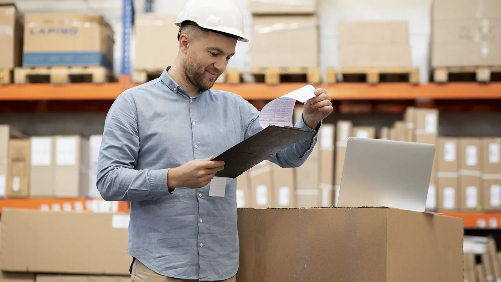 hombre revisando planilla en depósito rodeado de cajas